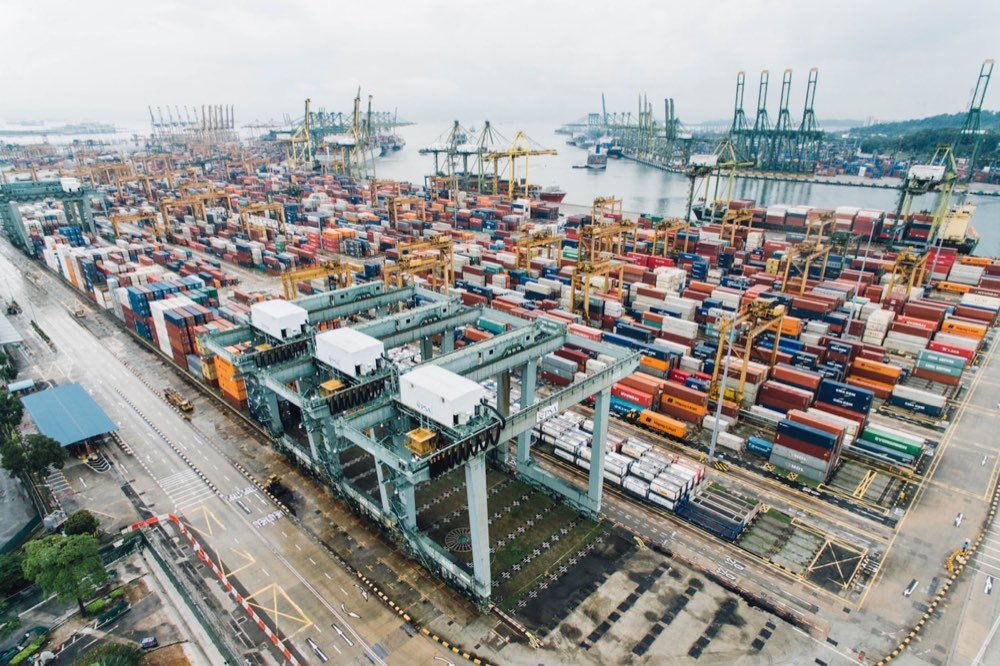 Aerial view of a container terminal with stacked containers, gantry cranes and berthed vessels.